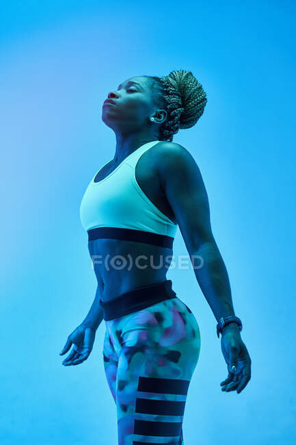 Young African American sportswoman with Afro braids in bun and closed eyes on blue background — Stock Photo