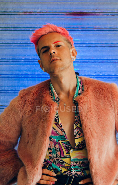 Молодой гомосексуалист в модной одежде с маникюром и современной стрижкой, смотрящий в камеру на синем фоне — стоковое фото