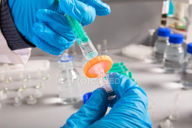 Crop unrecognizable biologist in latex gloves filling injector with liquid from small bottle in laboratory — Stock Photo