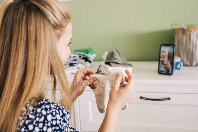 Вид збоку врожаю молода жінка, що показує дитячі шкарпетки подрузі з дитиною на екрані мобільного телефону під час відеодзвінка — стокове фото
