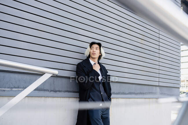 Giovane ben vestito etnico dirigente maschile con mano in tasca guardando lontano contro il muro della casa in città — Foto stock