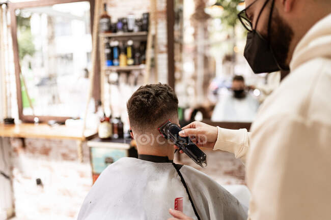 Male hairstylist in eyeglasses making haircut to adult client in hairdressing salon during COVID 19 pandemic — Fotografia de Stock