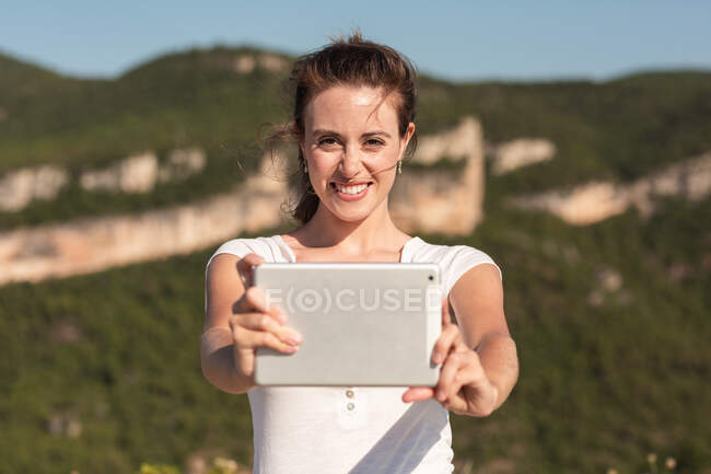 Задоволена жінка мандрівник взяла власний портрет на планшеті на фоні гірського хребта влітку — стокове фото