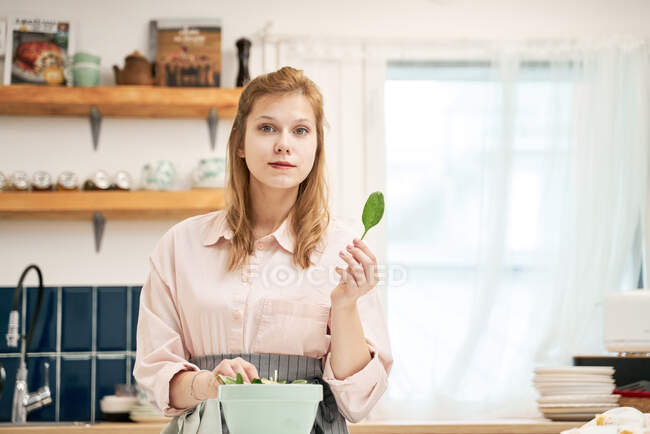 Женщина со шпинатной листвой над миской на столе во время приготовления пищи в доме — стоковое фото