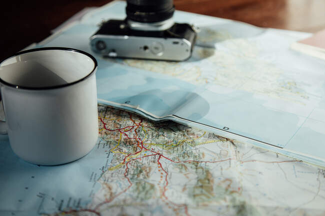 Vintage photo camera and metal mug of coffee on route map during trip — Foto stock