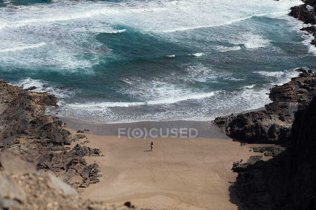 De cima vista traseira do viajante fêmea anônimo admirando o oceano espumoso da praia arenosa entre montanhas — Fotografia de Stock