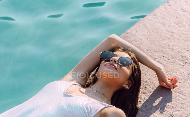 Junge weibliche Reisende in weißer Badebekleidung und moderner Sonnenbrille liegen an sonnigen Tagen am Pool — Stockfoto