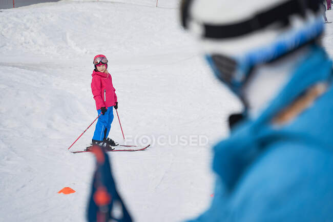 Side view faceless parent in warm sportswear and helmet teaching little kid to ski alongside snowy hill slope in winter ski resort — Stock Photo