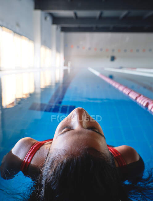 Молода жінка-спортсменка з закритими очима в купальнику, що плаває на спині в басейні з чистою акваріумом і брижами — стокове фото