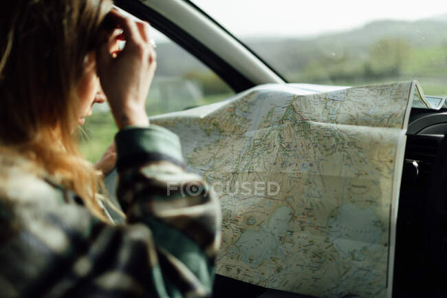 Side view of cropped focused female tourist looking at route map while sitting in automobile - foto de stock
