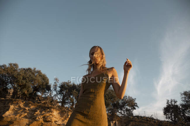 Von unten eine sinnliche blonde Frau, die in der Nähe eines sandigen Hangs mit Graspflanzen steht — Stockfoto
