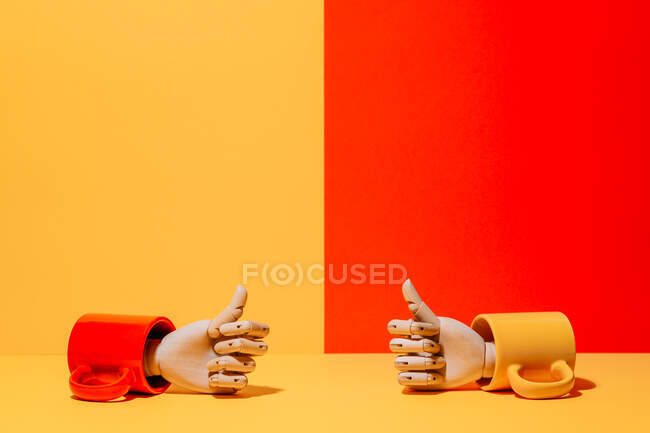 Mão de madeira ornamental criativa com polegares para cima dentro caneca colorida no fundo amarelo e vermelho no estúdio — Fotografia de Stock