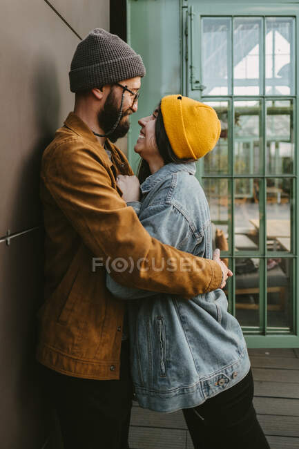 Side view of young stylish couple hugging gently while standing on wooden terrace near house — Stock Photo