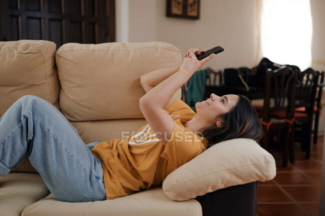 Вид збоку молодої жінки, взявши власний портрет на мобільний телефон, лежачи на дивані у вітальні — стокове фото