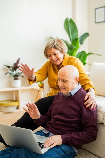 Cheerful mature couple talking on video chat on laptop and waving hands in living room — Stock Photo