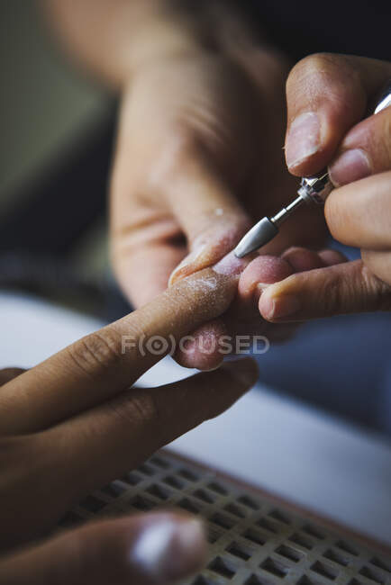 Crop unrecognizable female master using electric nail file while doing manicure for client in beauty salon — Stock Photo