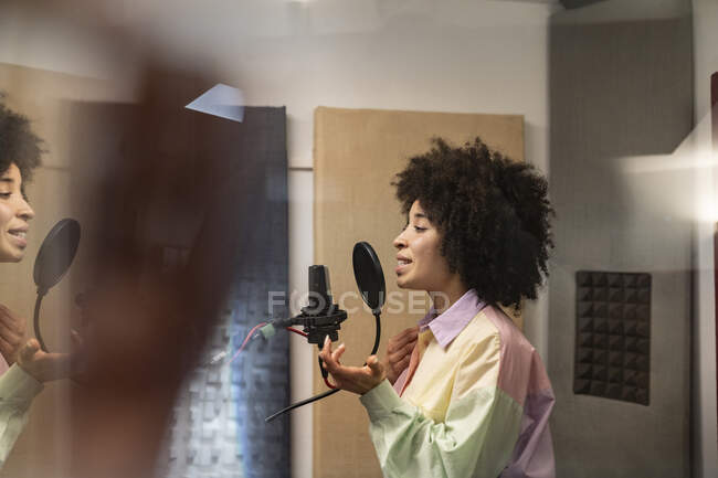 Vista laterale della giovane cantante afroamericana che canta in microfono con filtro pop in studio di registrazione — Foto stock