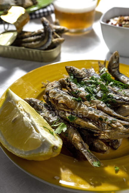 From above of delicious fried anchovies served on plates with lemon and placed on white table with glass of beer — Foto stock
