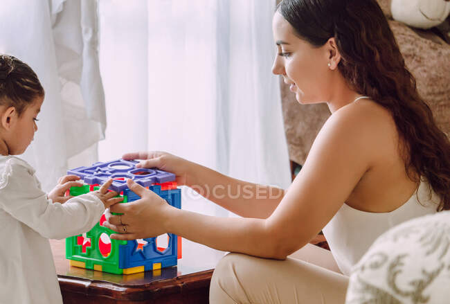 Vue latérale de la femme ethnique et de la petite fille jouant ensemble avec un jouet d'apprentissage à la maison — Photo de stock