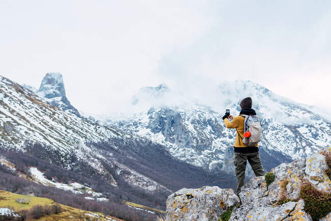Voltar ver turista corpo inteiro feminino com mochila usando smartphone enquanto fotografa incrível natureza de Peaks da Europa durante a viagem — Fotografia de Stock