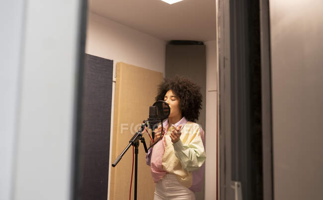 Cantora negra cantando música contra microfone com filtro pop em pé e olhos fechados no estúdio de som — Fotografia de Stock