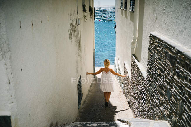 Back view of anonymous carefree female tourist with raised arms walking on narrow street between old buildings in city — Foto stock