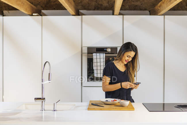 Side view of cheerful female surfing internet on cellphone while sitting on table in loft style house — Stock Photo
