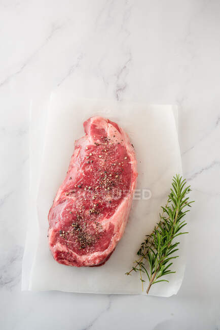 Vue aérienne de la pièce de viande non cuite avec des feuilles de thym contre du papier cuisson sur fond de marbre — Photo de stock