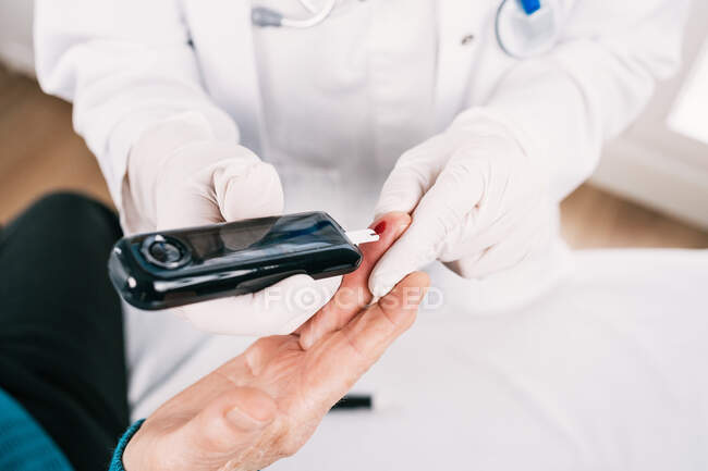 Alto ángulo de cultivo médico anónimo tomar análisis de sangre del paciente con dispositivo médico en la clínica - foto de stock