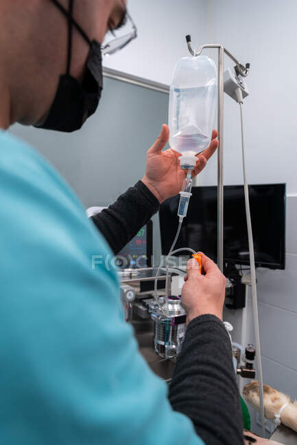Side view of crop male vet in cloth face mask with medical dropper against pet after surgery in clinic — Stock Photo