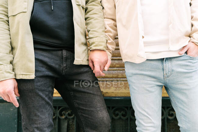 Crop young multiethnic gays in stylish clothes holding hands on city street - foto de stock