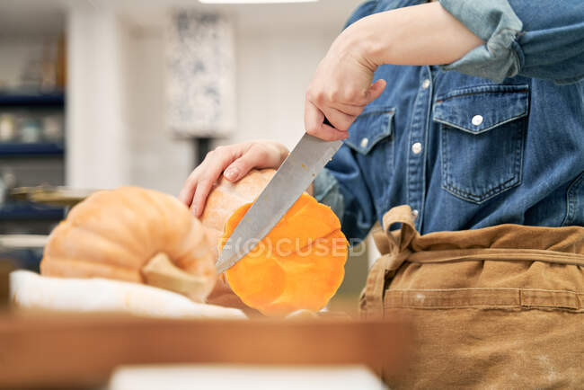 Crop female with sharp knife cutting raw squash on chopping board while cooking in kitchen at home — Stock Photo