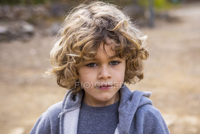 Charming child in soft gray wear looking away on blurred background in daylight outdoors — Photo de stock