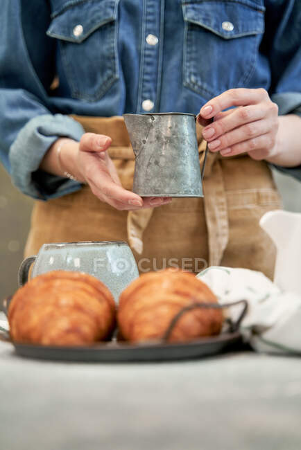 Jeune blogueuse versant du lait de cruche à table avec des croissants à la maison — Photo de stock