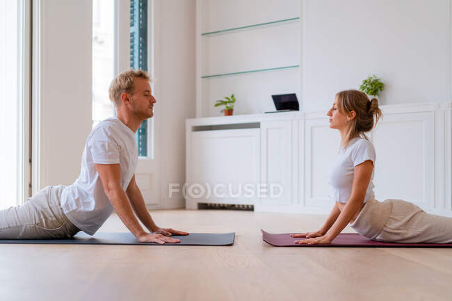 Ground level side view of serene couple practicing yoga in Bhujangasana in morning at home - foto de stock