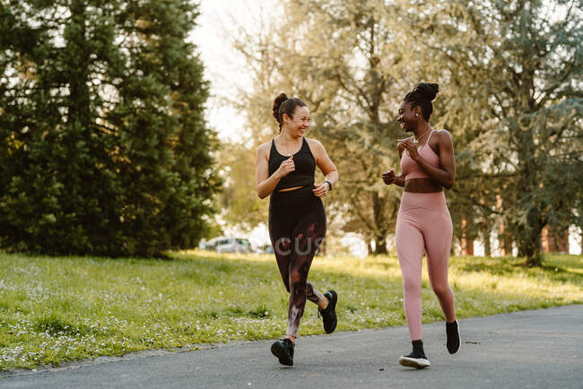 Sorrindo multirraciais corredores do sexo feminino em activewear jogging e falando durante o treinamento cardio na passarela na cidade — Fotografia de Stock