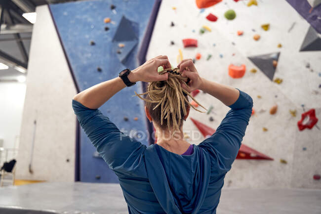 Back view of anonymous female mountaineer with dreadlocks standing in bouldering gym with artificial wall — Stock Photo