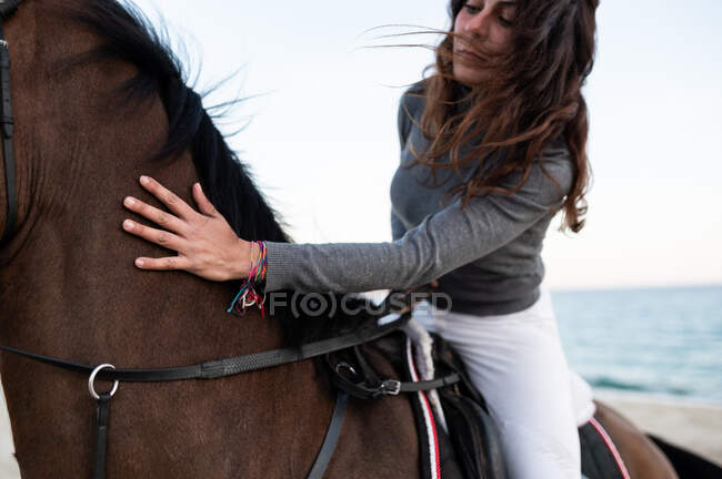 Young female riding chestnut horse on sandy sea shore against mount under light sky — Stock Photo