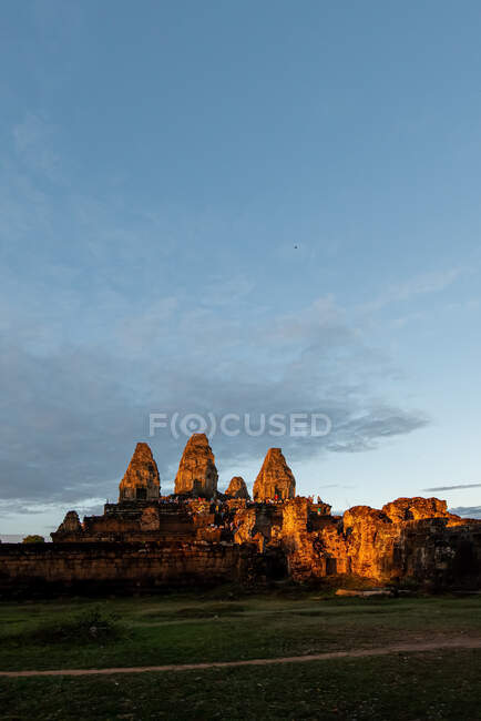 Vecchio tempio di pietra esterno complesso contro prato sotto il cielo blu in Cambogia in serata — Foto stock
