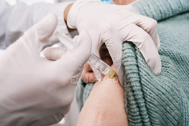 Crop medic in uniform with syringe vaccinating patient during coronavirus pandemic in clinic — Stock Photo