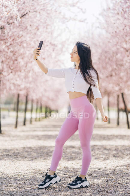 Молода ніжна жінка бере селфі з мобільним телефоном, стоячи в парку — стокове фото
