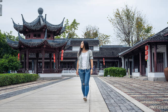 Belle femme asiatique marchant dans un jardin chinois avec une architecture traditionnelle en arrière-plan — Photo de stock