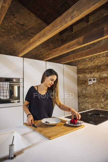 Content female with knife cutting ripe strawberry while preparing healthy food in bowl at home — Stock Photo