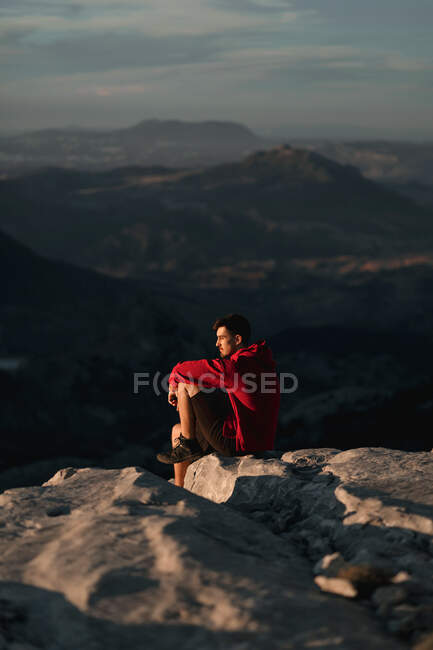 Side view of thoughtful male hiker in casual wear resting on rocky mountain summit and admiring scenic views over rough highlands in Seville Spain — Stock Photo