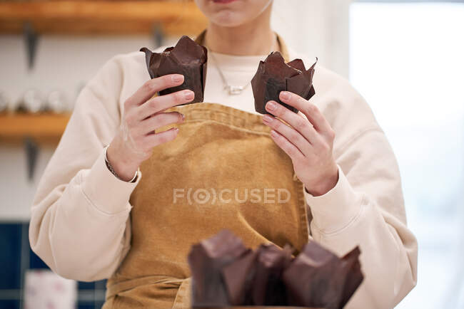 Crop unrecognizable female in apron showing baked dessert in paper liners in house kitchen — Stock Photo