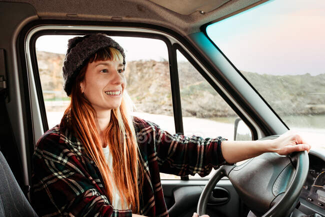 Sonriente mujer hipster viajera sentada en el asiento del conductor en un camión estacionado en las tierras altas - foto de stock