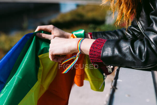 Seitenansicht der Ernte anonyme lesbische Frau in Regenbogenarmband steht mit bunten LGBT-Flagge in der Stadt an sonnigen Tag — Stockfoto