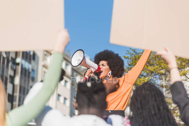 African American female social justice warrior with speaker against crop anonymous multiracial people with placards fighting for human rights in town — Photo de stock