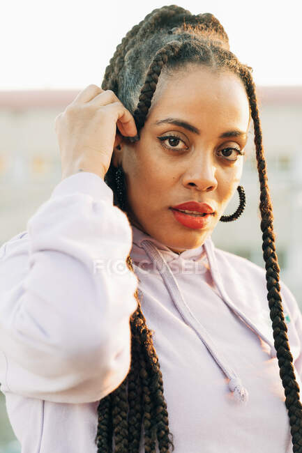 Jeune femme afro-américaine avec des lèvres rouges et des tresses afro regardant la caméra en plein air — Photo de stock