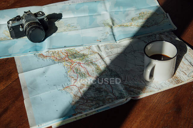 Top view of vintage photo camera and metal mug of coffee on route map during trip — Stock Photo